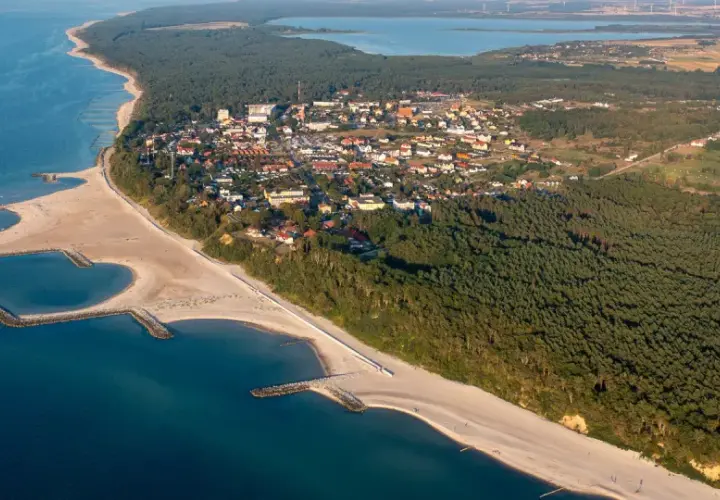 Jarosławiec atrakcje: malownicza plaża z falochronami, lasy sosnowe i zabudowania kurortu nad Bałtykiem.