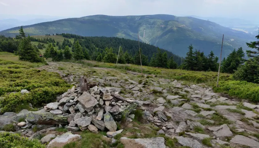 Kamienny szlak i kopczyk na górskim szczycie. W oddali widać zalesione pasma górskie, idealne miejsce na odkrywanie międzylesie atrakcje.