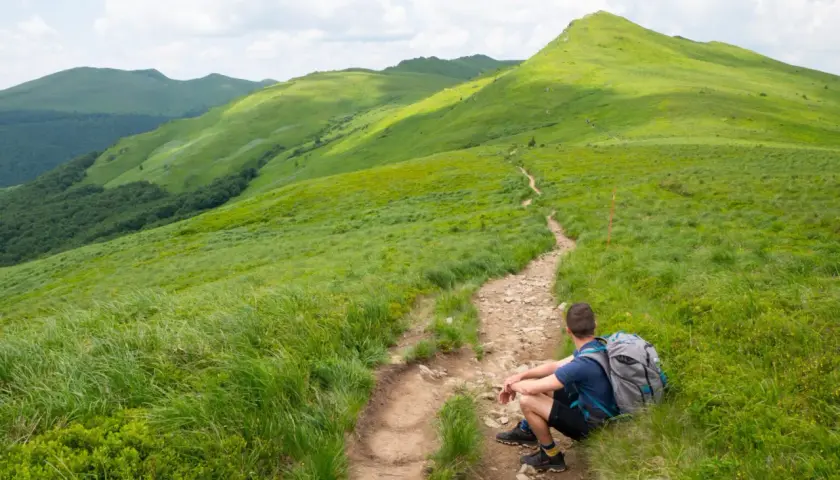 Turysta odpoczywa na szlaku, podziwiając zielone połoniny. Bieszczady atrakcje czekają!