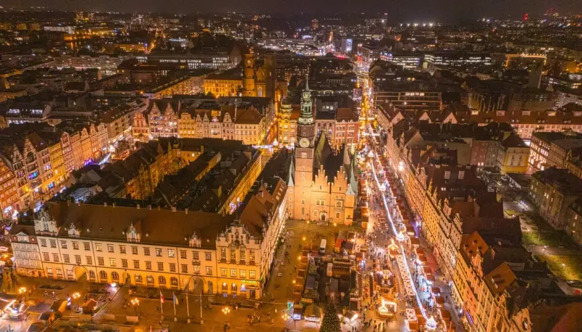 Nocny widok na Wrocławski Rynek, gdzie tętni życiem największy jarmark bożonarodzeniowy w Polsce. Kolorowe iluminacje i tłumy ludzi tworzą magiczną atmosferę.