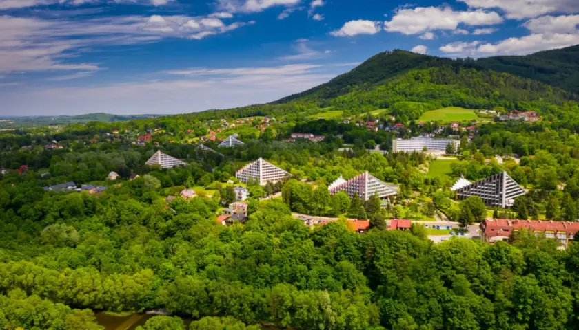 Ustroń atrakcje: widok z lotu ptaka na zielone wzgórza Beskidów, charakterystyczne budynki w kształcie piramid i inne obiekty architektoniczne.
