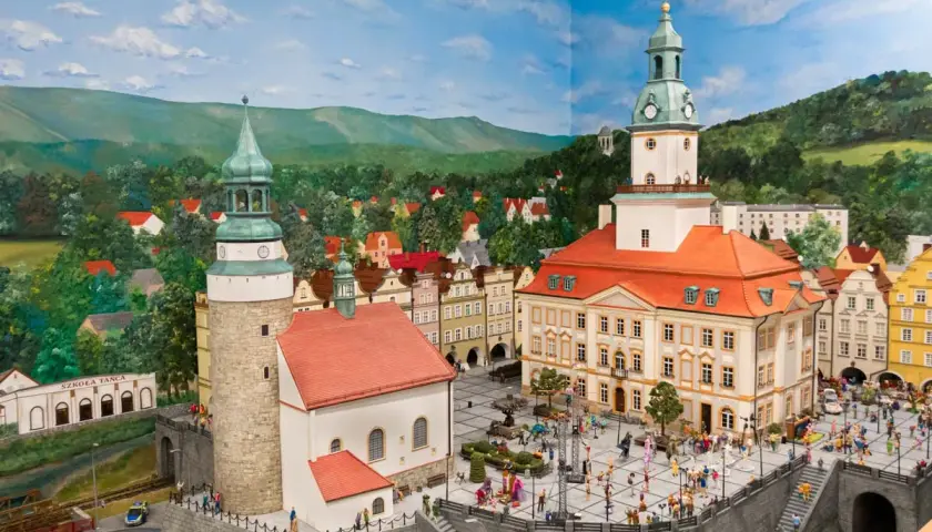 Miniaturowa panorama miasta z wieżami i placem pełnym ludzi. W tle góry i lasy, idealne na odkrywanie atrakcji w okolicy Jeleniej Góry.