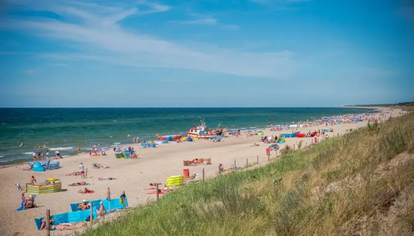 Słoneczna plaża w Dąbkach pełna turystów, kolorowych parawanów i łodzi. Idealne miejsce na wakacyjne atrakcje nad Bałtykiem.