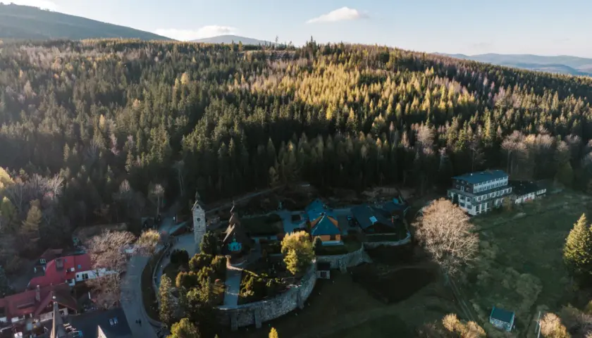 Kolorowy kompleks budynków, w tym hotel i kościółek, otoczony lasem. To idealne miejsce na **centrum rekreacji i sportu**, gdzie można odpocząć wśród natury.