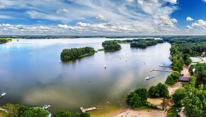 Idealne wakacje nad wodą: żaglówki, wyspy porośnięte drzewami i plażowicze cieszący się słońcem.