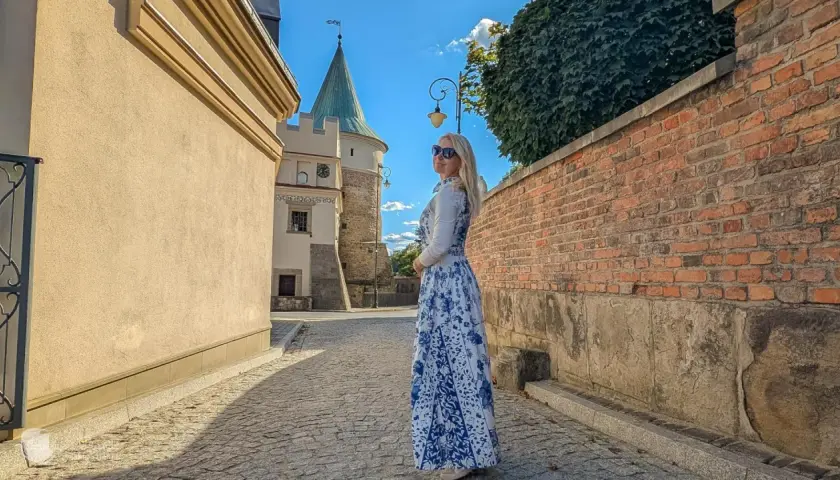 Kobieta w sukience w kwiaty podziwia biecz atrakcje. W tle zamek i brukowana uliczka.