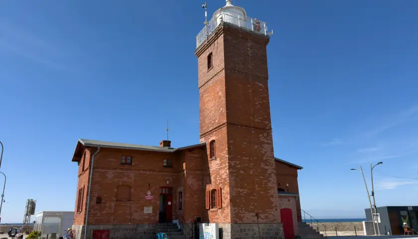 Latarnia morska w Darłowie, jedna z głównych atrakcji, góruje nad ceglanym budynkiem.