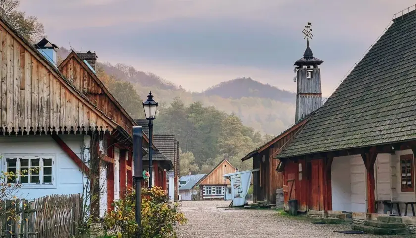 Sanok atrakcje: skansen z drewnianymi domami i wieżą, otoczony mglistymi wzgórzami.