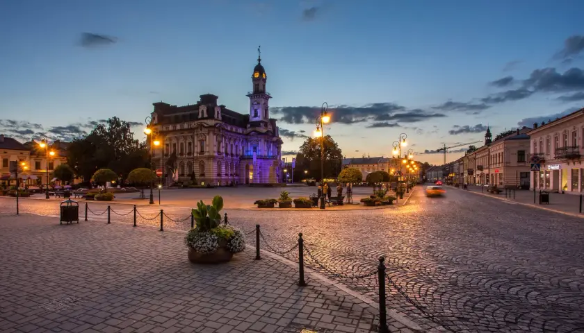 Wieczorny rynek w Nowym Sączu, oświetlony latarniami i iluminacją ratusza. Brukowana nawierzchnia i zabytkowa architektura tworzą niepowtarzalny klimat, zachęcając do odkrywania atrakcji Nowego Sącza.
