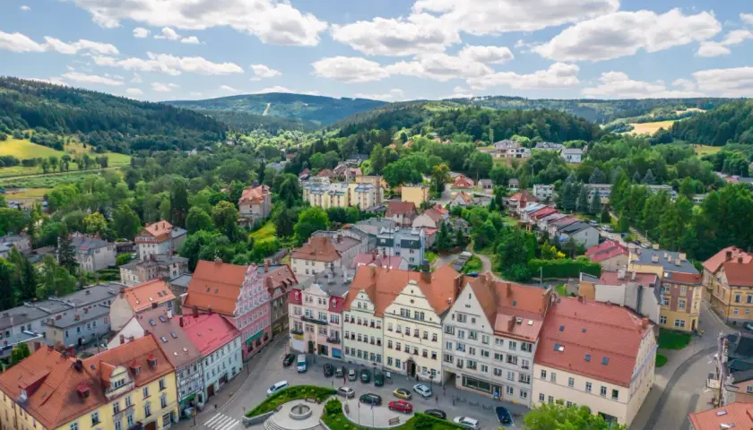 Urokliwy rynek i kolorowe kamienice w Dusznikach Zdroju. W tle zielone wzgórza, idealne na piesze wycieczki i odkrywanie atrakcji.