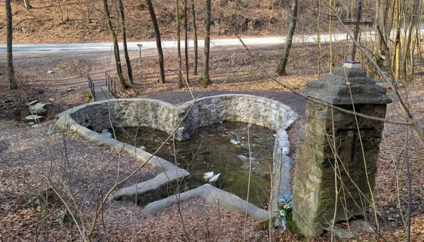 Kamienny krzyż i sercowate źródełko w dolinie Eliasówki, otoczone jesiennym lasem.