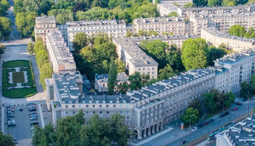 Osiedle bloków mieszkalnych w stylu socrealistycznym, z zielenią i ulicą, przypomina architekturę Nowej Huty.