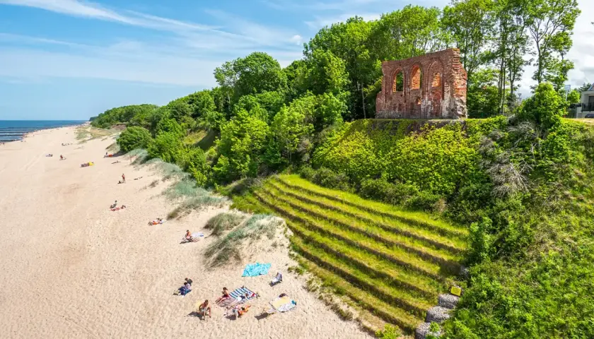 Piękna plaża z ruinami na klifie, zielone tarasy i ludzie odpoczywający na piasku. Trzęsacz atrakcje zachwycają!