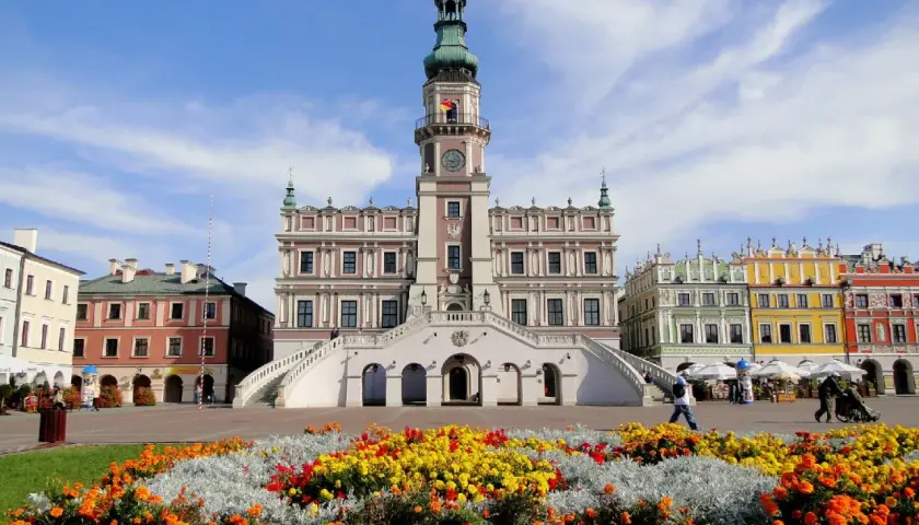 Zamość atrakcje: Ratusz i kolorowe kamienice na Rynku Wielkim, otoczone kwitnącymi rabatami.