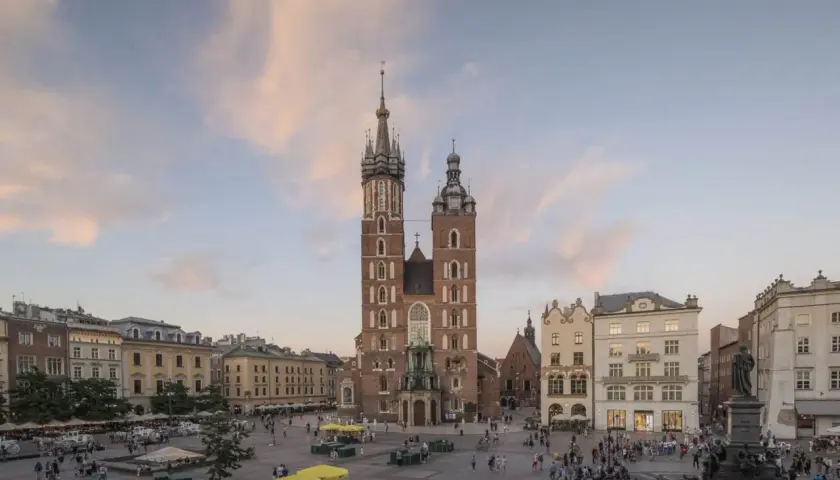 Majestatyczny kościół Mariacki na Rynku Głównym w Krakowie, otoczony kamienicami i placem tętniącym życiem.