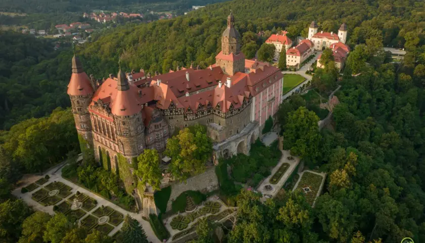 Zamek Książ otoczony lasami, z malowniczymi ogrodami i pobliską wsią. Rudawy Janowickie w tle.