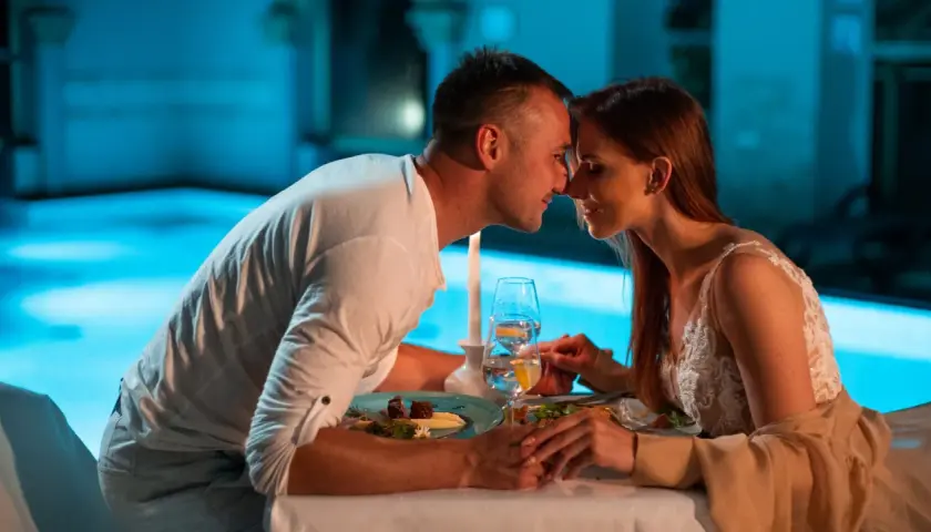 Romantyczna kolacja przy basenie, idealne fajne miejsca na sylwestra we dwoje. Para trzyma się za ręce, patrząc sobie w oczy.