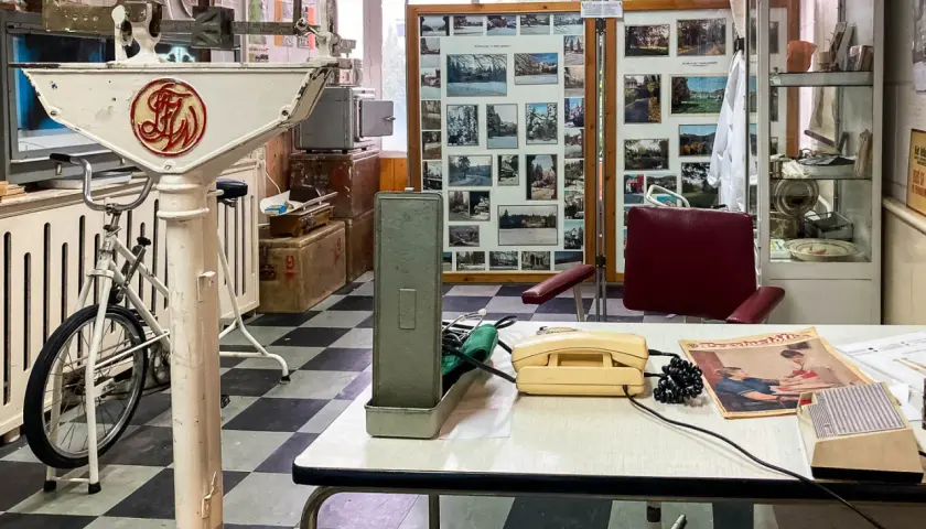 Wnętrze gabinetu lekarskiego z lat 70. XX wieku, część ekspozycji muzeum Dolny Śląsk. Widoczna waga lekarska, rower, aparat telefoniczny i zdjęcia.
