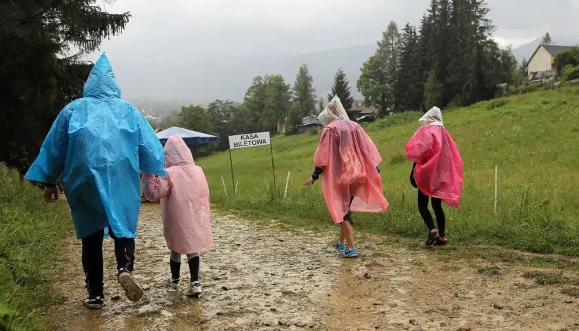 Rodzina w kolorowych pelerynach idzie błotnistą ścieżką. Nawet gdy pada deszcz, w Zakopanem można znaleźć ciekawe atrakcje.