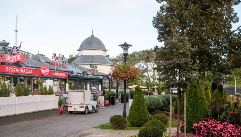 Ulica w Międzyzdrojach z restauracjami i kawiarniami, zielenią i ozdobnymi krzewami. Idealne miejsce na spacer i odkrywanie międzyzdrojskich atrakcji.