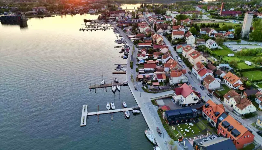 Zachód słońca nad jeziorem w Mikołajkach. Widok na port z łodziami i urokliwe miasteczko z czerwonymi dachami. Idealne miejsce na wakacyjne mikołajki atrakcje.