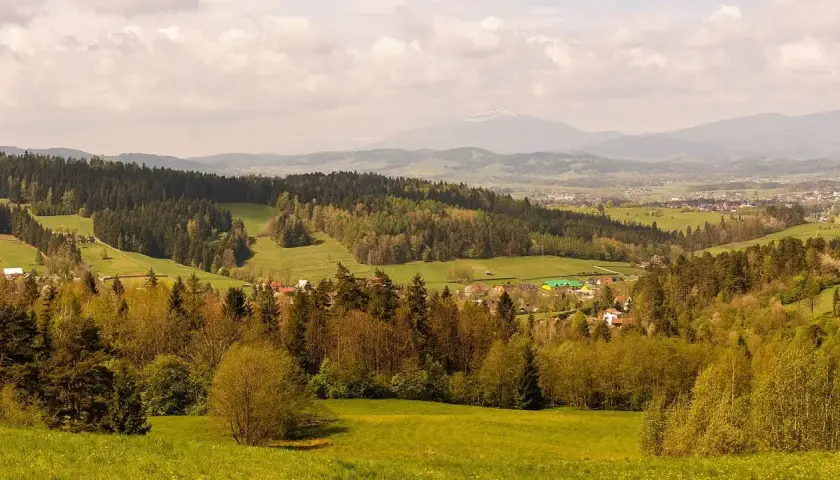 Malowniczy krajobraz z lasami i polami, w oddali widać góry i zabudowania. To idealne miejsce na odkrywanie rabka-zdrój atrakcje.