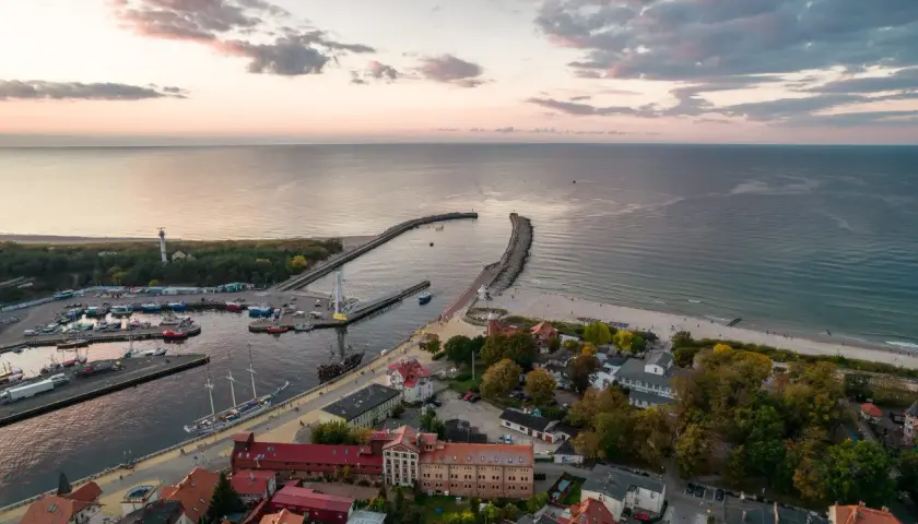 Widok na port i plażę w Ustce. Widać łodzie, latarnię morską i zabudowania. To jedne z wielu ustka atrakcje.