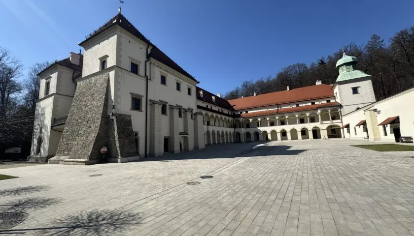 Zamek w Suchej Beskidzkiej, z dziedzińcem wyłożonym kamienną kostką i arkadowymi krużgankami, prezentuje się majestatycznie pod błękitnym niebem.