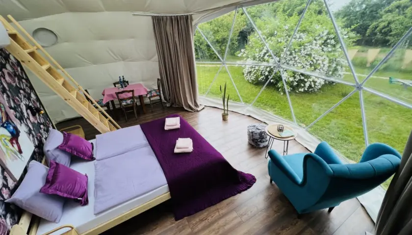 Przytulne wnętrze namiotu sferycznego z wygodnym łóżkiem i widokiem na zieleń. Idealne miejsce na glamping w Nałęczowie.