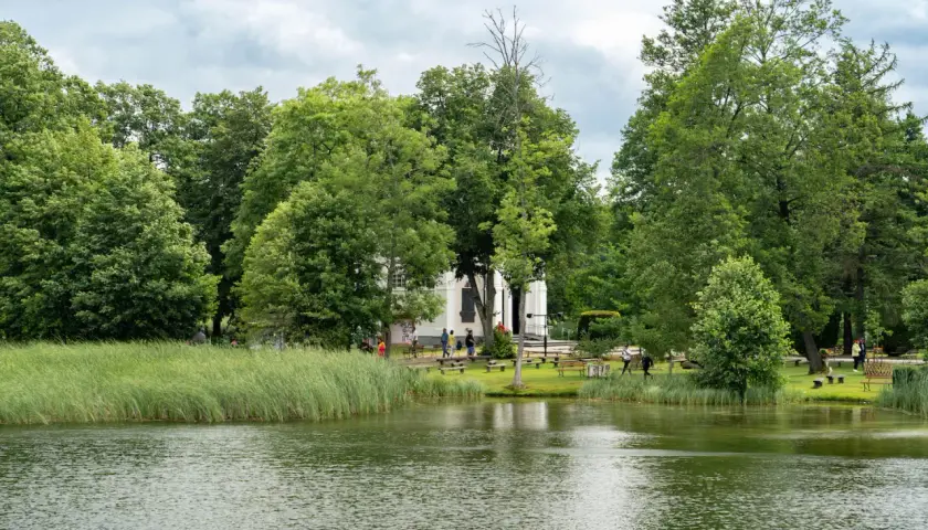 Malownicze jezioro i zielone tereny wokół białego budynku, idealne na spacer. Augustów atrakcje zachęcają do odpoczynku na łonie natury.