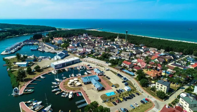 Widok z lotu ptaka na Dziwnów: port jachtowy, domy, las i morze. Wiele łodzi zacumowanych w marinie, idealne miejsce na wakacje.