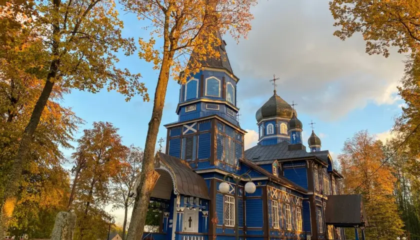 Jesienna odsłona cerkwi na Podlasiu. Złote liście i błękitne niebo podkreślają piękno drewnianej architektury, tworząc malownicze podlaskie atrakcje.
