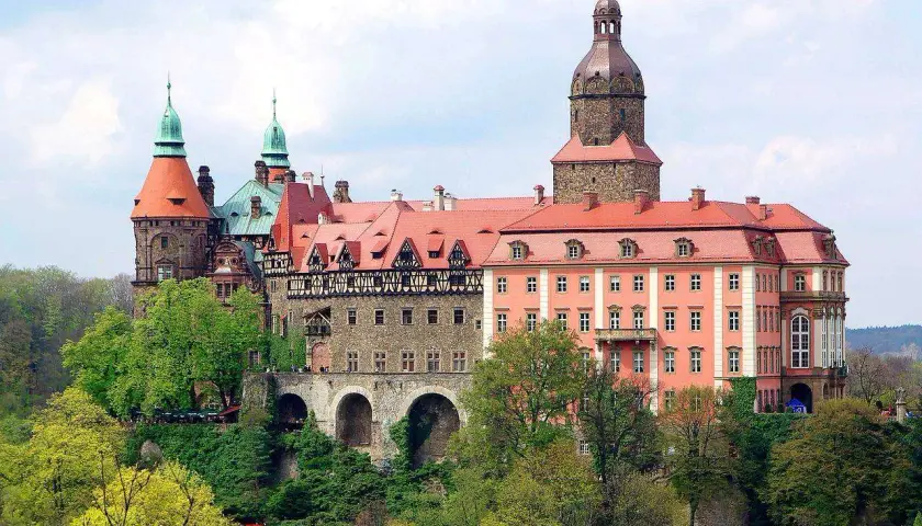 Imponujące zamki w okolicy Wrocławia, z wieżami i czerwonymi dachami, otoczone zielenią.
