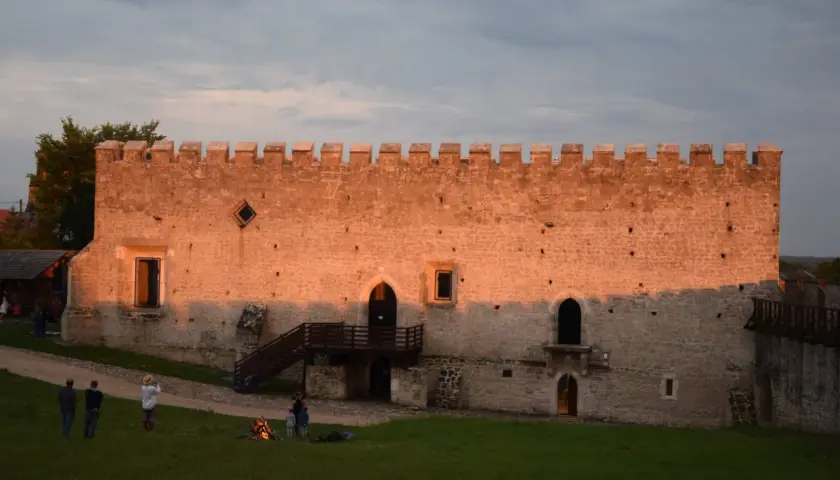 Zamek w Szydłowie o zachodzie słońca. Ludzie odpoczywają na trawie, podziwiając historyczne atrakcje.