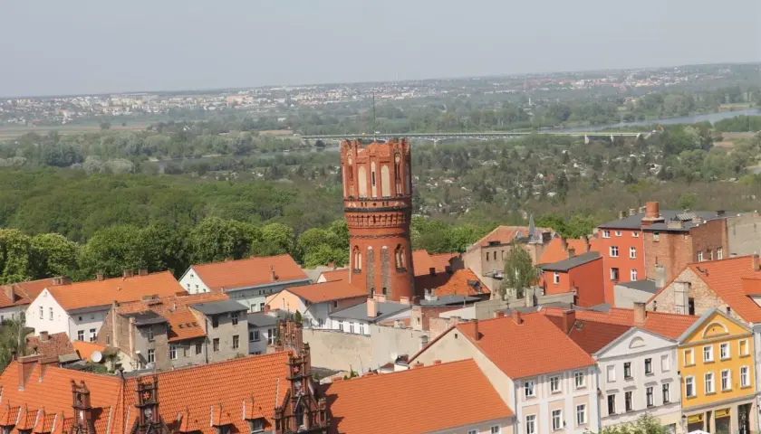 Widok na Chełmno z charakterystyczną wieżą ciśnień. Miasto z czerwonymi dachami i zielenią w tle. Chełmno atrakcje warte zobaczenia.