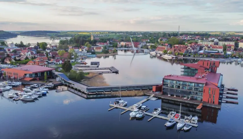 Malownicze mazury miejscowości z nowoczesną architekturą nad jeziorem, pełne łodzi i jachtów.