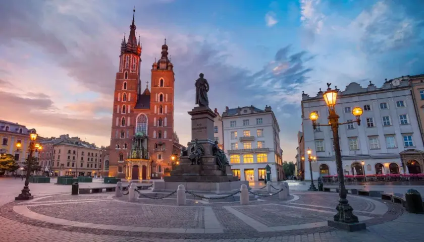 Kraków co zwiedzić? Rynek Główny z Kościołem Mariackim i pomnikiem Mickiewicza o zachodzie słońca. Idealne miejsce na spacer.