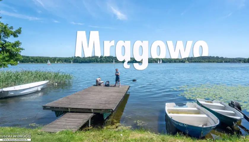 Mrągowo atrakcje: spokojny dzień nad jeziorem, dzieci łowią ryby z pomostu, żaglówki na horyzoncie.