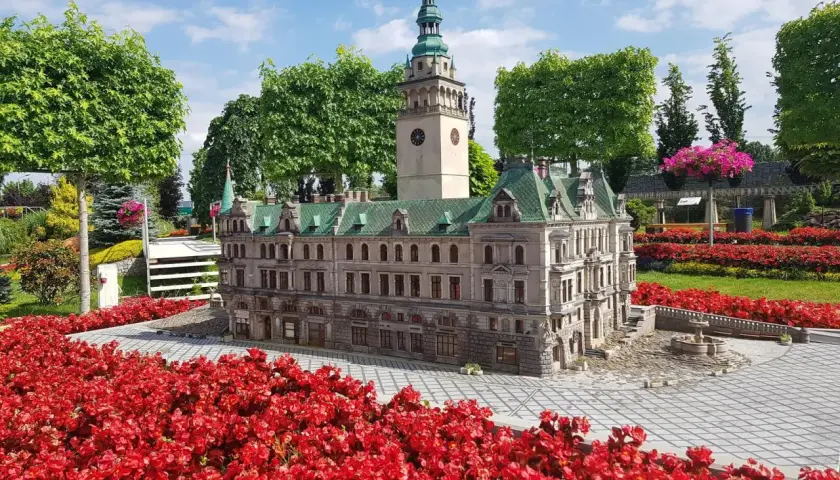 Miniatura ratusza z wieżą i zegarem, otoczona czerwonymi kwiatami. Jedna z wielu kłodzko atrakcje.