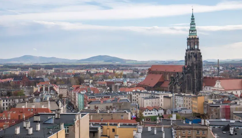 Widok na miasto z dominującą wieżą kościoła. W oddali góry. **Świdnica atrakcje** zachwycają.