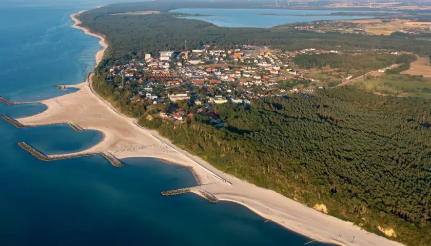 Jarosławiec atrakcje: malownicza plaża z falochronami, lasy sosnowe i zabudowania kurortu nad Bałtykiem.