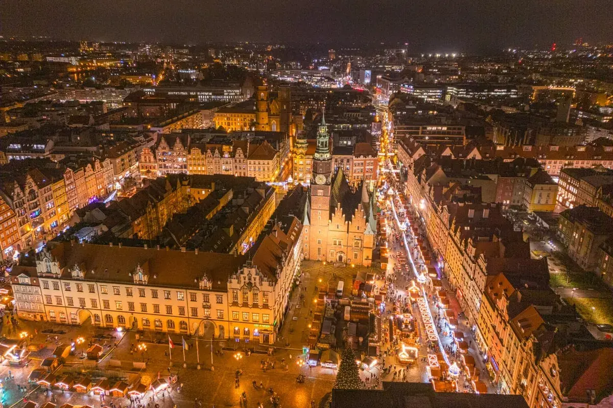 Nocny widok na Wrocławski Rynek, gdzie tętni życiem największy jarmark bożonarodzeniowy w Polsce. Kolorowe iluminacje i tłumy ludzi tworzą magiczną atmosferę.
