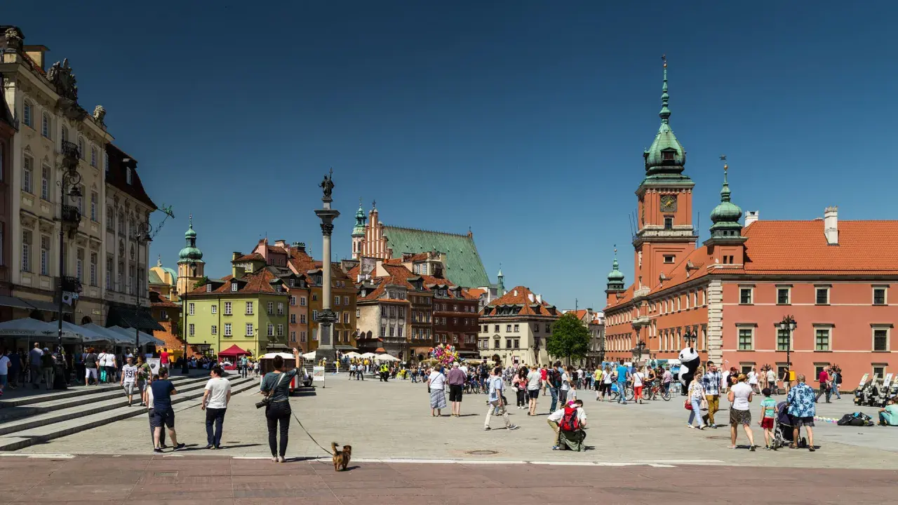 Warszawski Rynek Starego Miasta tętni życiem. Widać tu wiele zabytków w Polsce, w tym Zamek Królewski i Kolumnę Zygmunta.