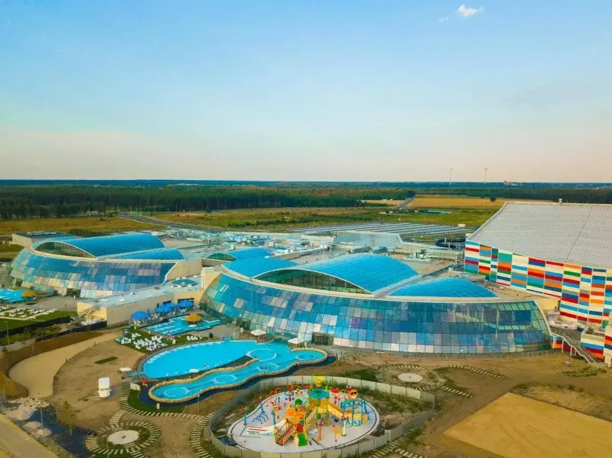 Nowoczesny park wodny Suntago z przeszklonymi dachami i kolorową fasadą, otoczony zielenią.