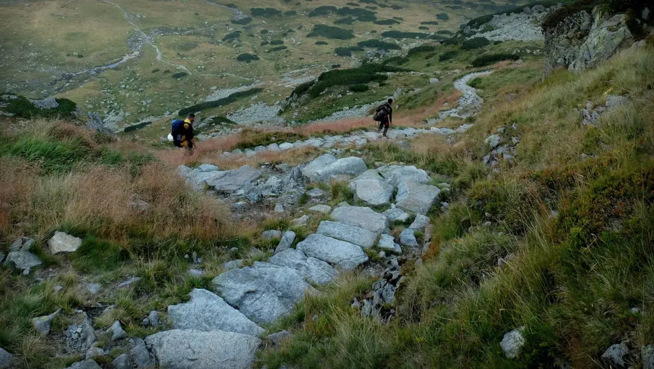 Dwóch turystów wędruje kamienistym szlakiem po zboczu górskim. Tatry atrakcje to wspaniałe widoki i wyzwania dla każdego miłośnika gór.