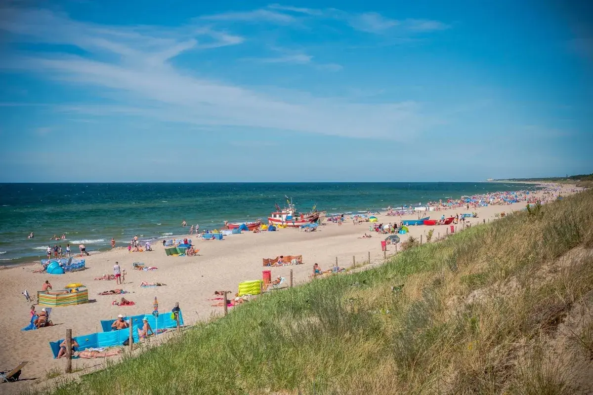 Słoneczna plaża w Dąbkach pełna turystów, kolorowych parawanów i łodzi. Idealne miejsce na wakacyjne atrakcje nad Bałtykiem.