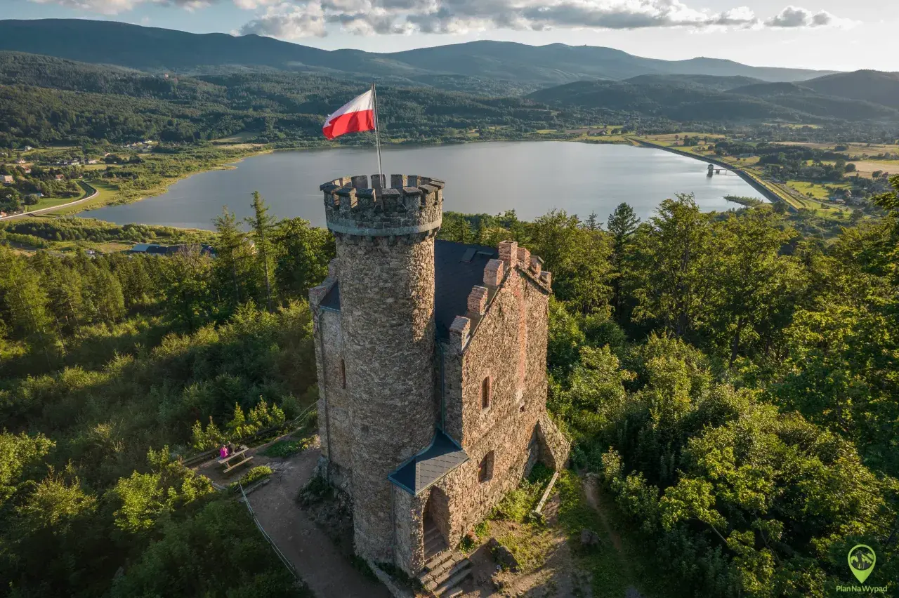Kamienna wieża z polską flagą na szczycie, w tle jezioro i góry. Idealne miejsce, by odkryć, co warto zobaczyć w Sudetach.