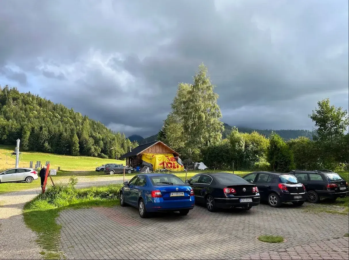 Samochody na parkingu pod Babią Górą, w tle las i chmury.