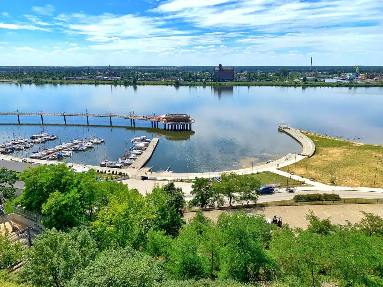 Nowoczesna marina i promenada nad rzeką, z widokiem na miasto. To jedne z wielu **ciekawych miejsc na Mazowszu**, idealnych na letni wypoczynek.