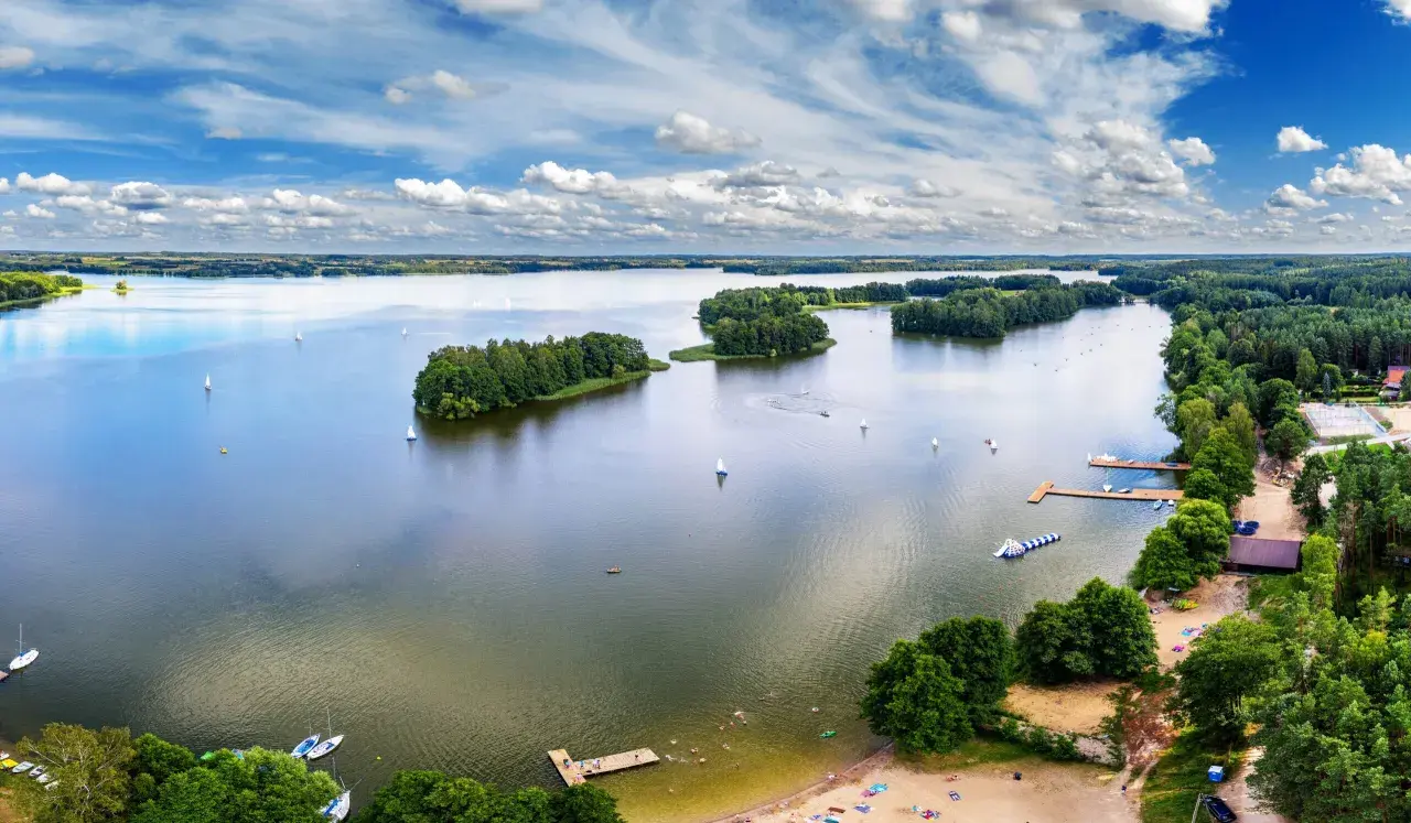 Idealne wakacje nad wodą: żaglówki, wyspy porośnięte drzewami i plażowicze cieszący się słońcem.